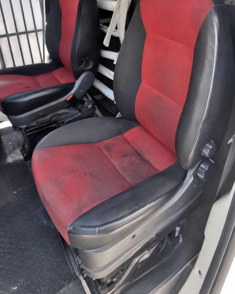Van front seats with dark grime and stains on the red fabric before valet