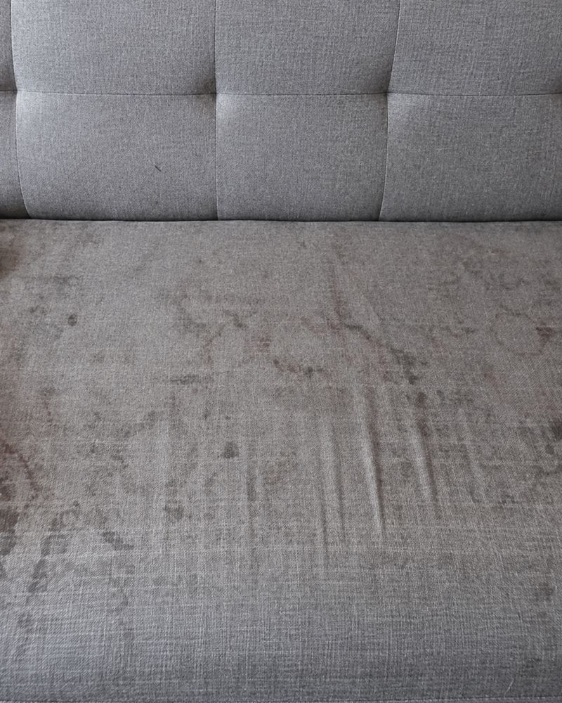 Grey fabric couch seat covered in dark water marks and stains before cleaning